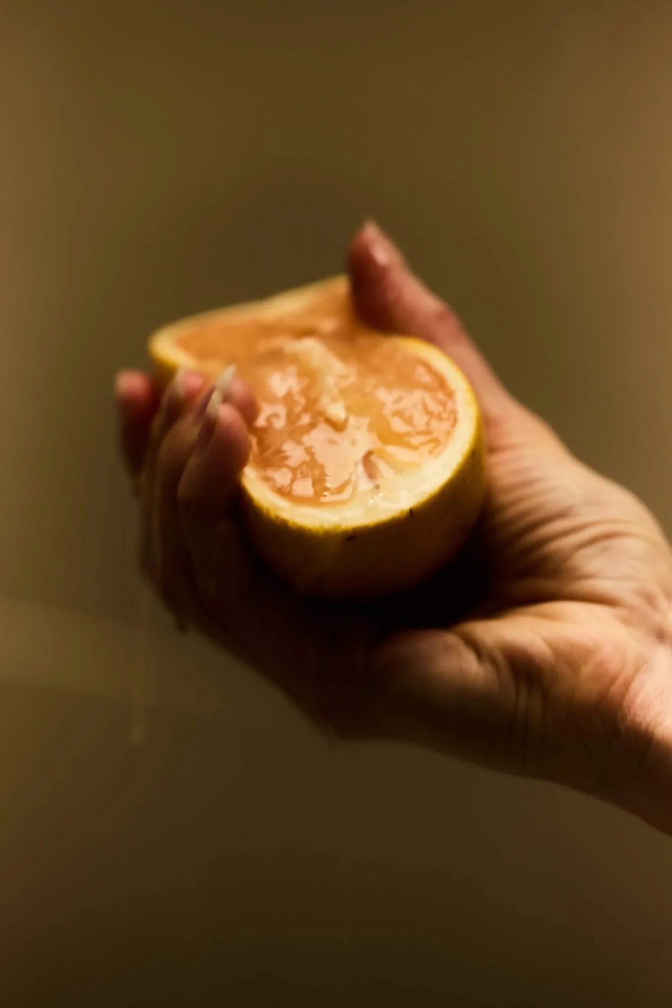 Hand holding a halved grapefruit against a neutral background