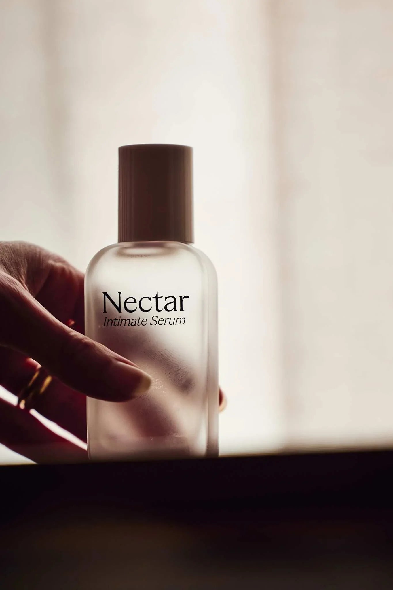 Bottle of 'Nectar Intimate Serum' held by a hand with a blurred background