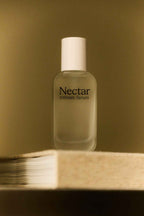 Bottle of 'Nectar Intimate Serum' on a wooden surface with a beige background